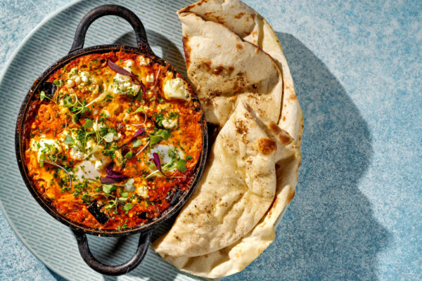 Shakshuka dish in a cast iron , two-handled skillet served with a large crescent-shaped pita bread. Naxos Taverna